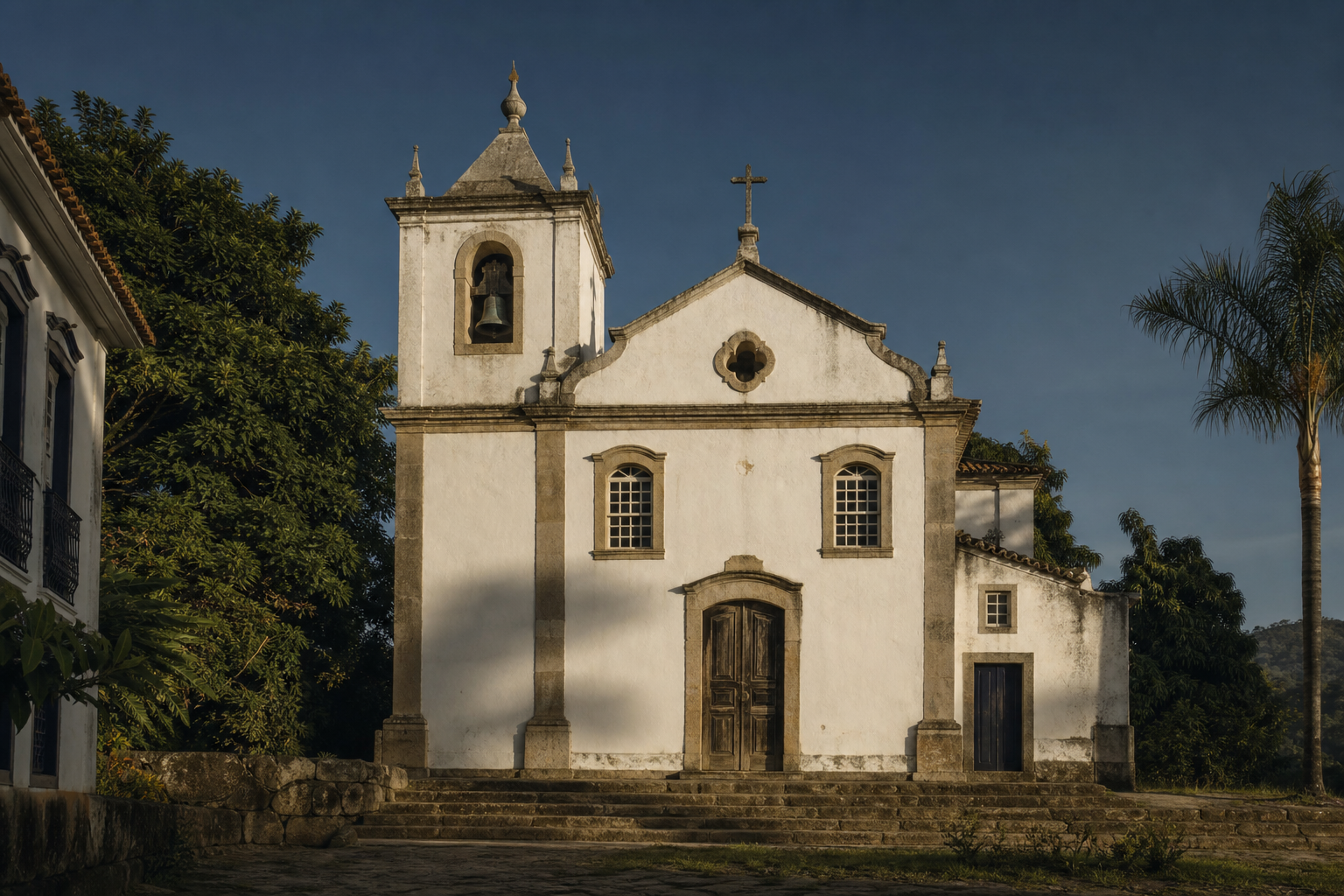 Capela colonial branca com torre simples e portas de madeira em praça silenciosa.
